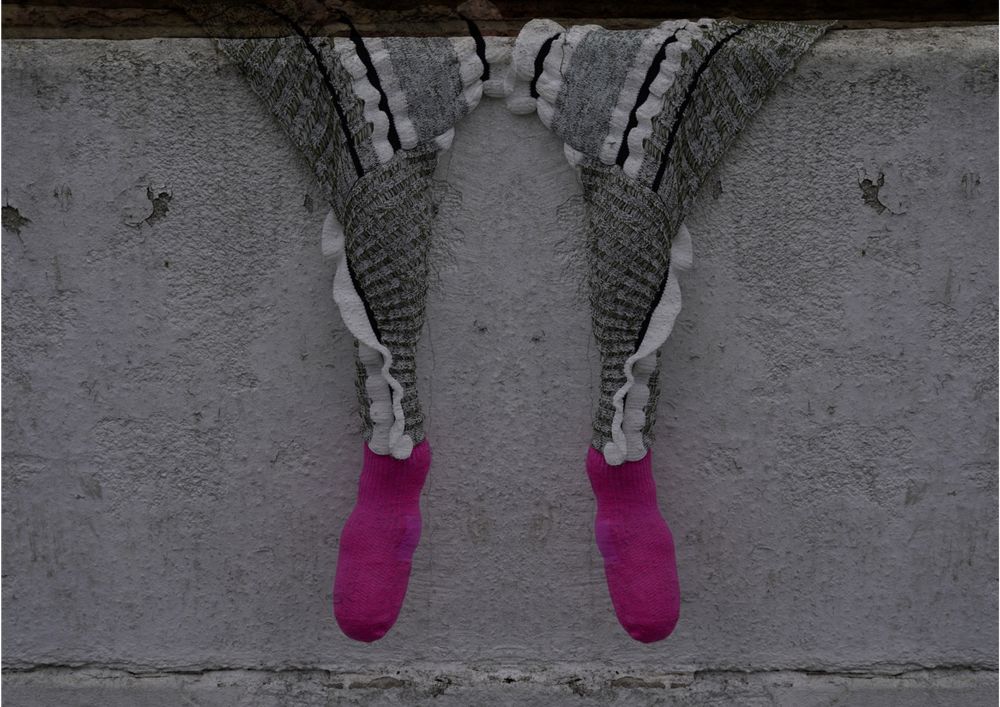 Knitted trousers draped over a stone wall, tucked into pink socks.