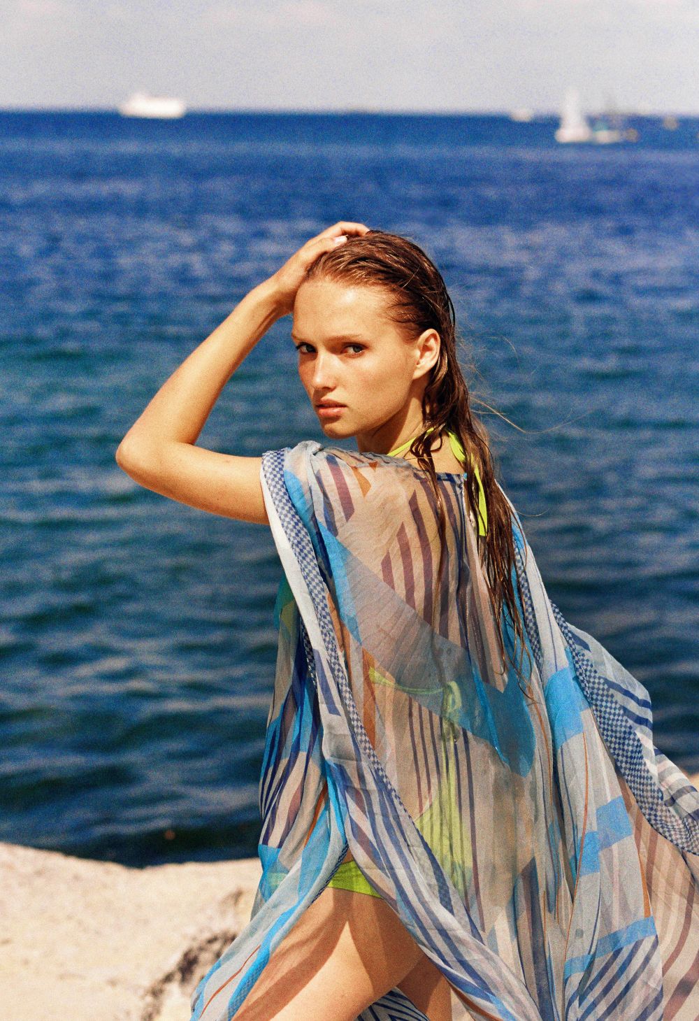 Woman on a rock in the Gia Sunray pleated kaftan with the sea behind her