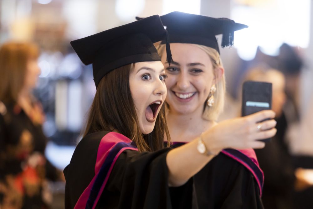 Two female graduates taking a selfie with smart phone.