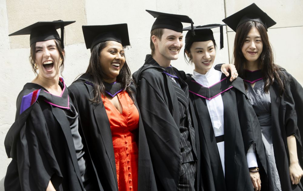 Five mixed graduates posing for a photograph side by side