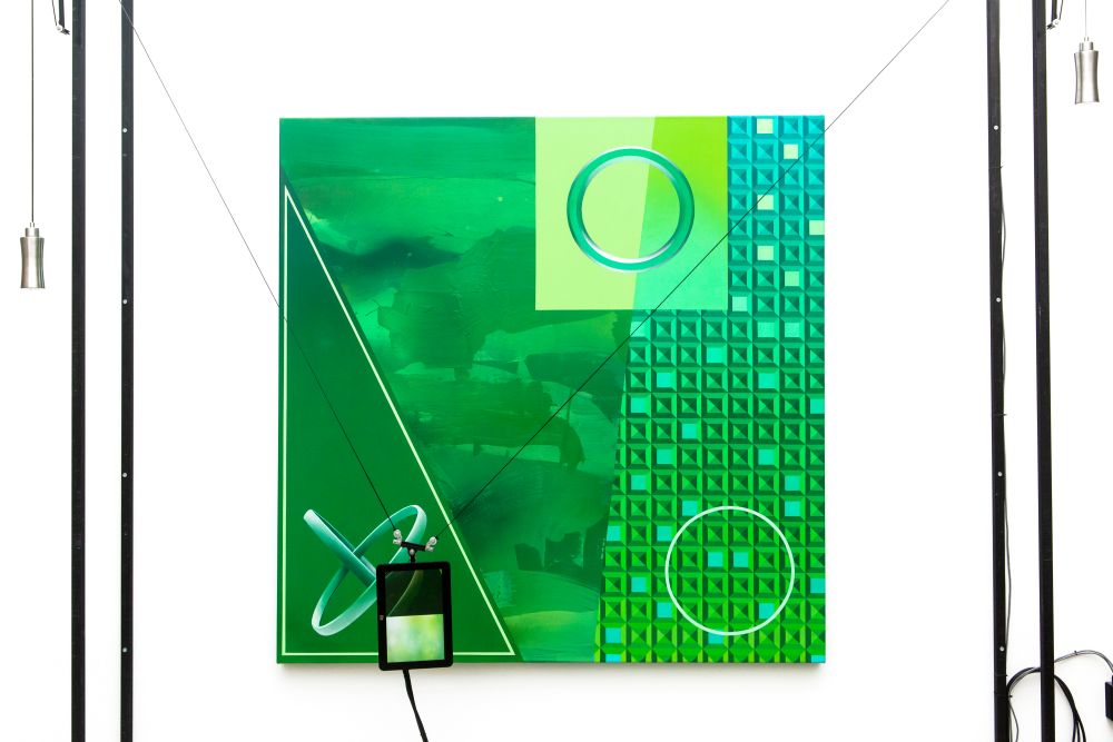 An installation including a green painting with an ipad hanging from wires in front of it.