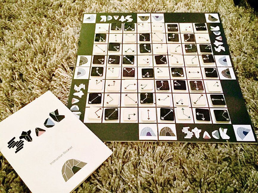 View of a board game. A black and white board divided into smaller squares. On each square is an image of a clock face without numbers. Around the edge are the words 'stack'