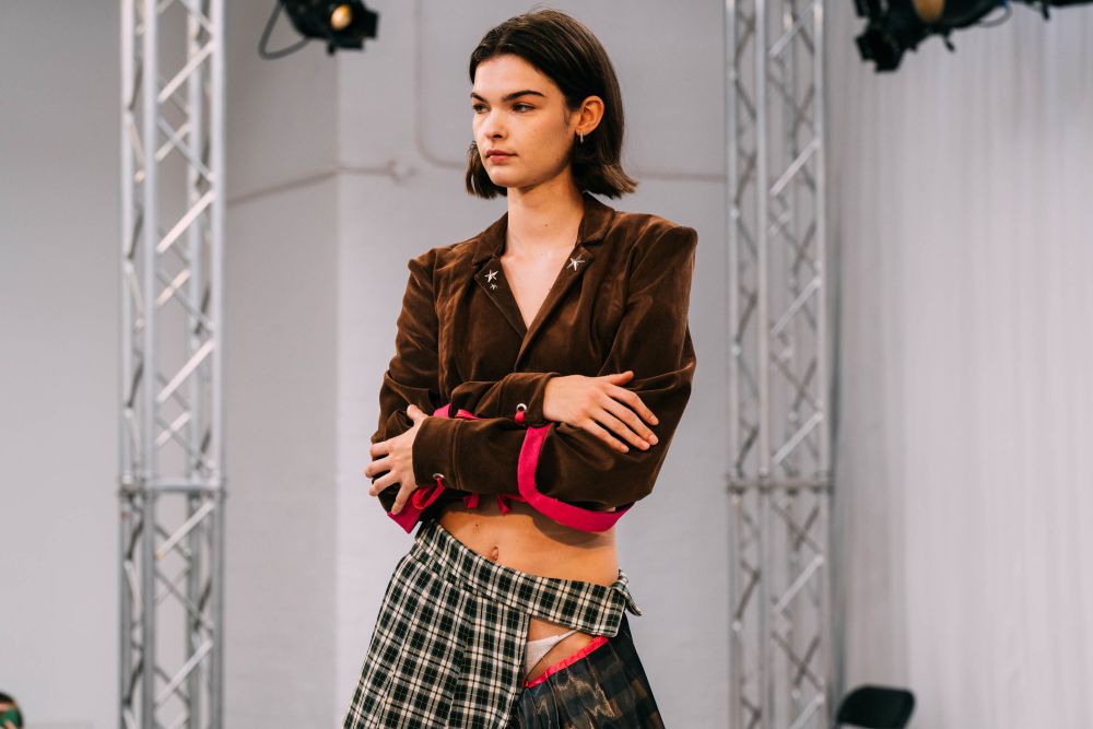Model on stage wearing brown blazer with their arms folded