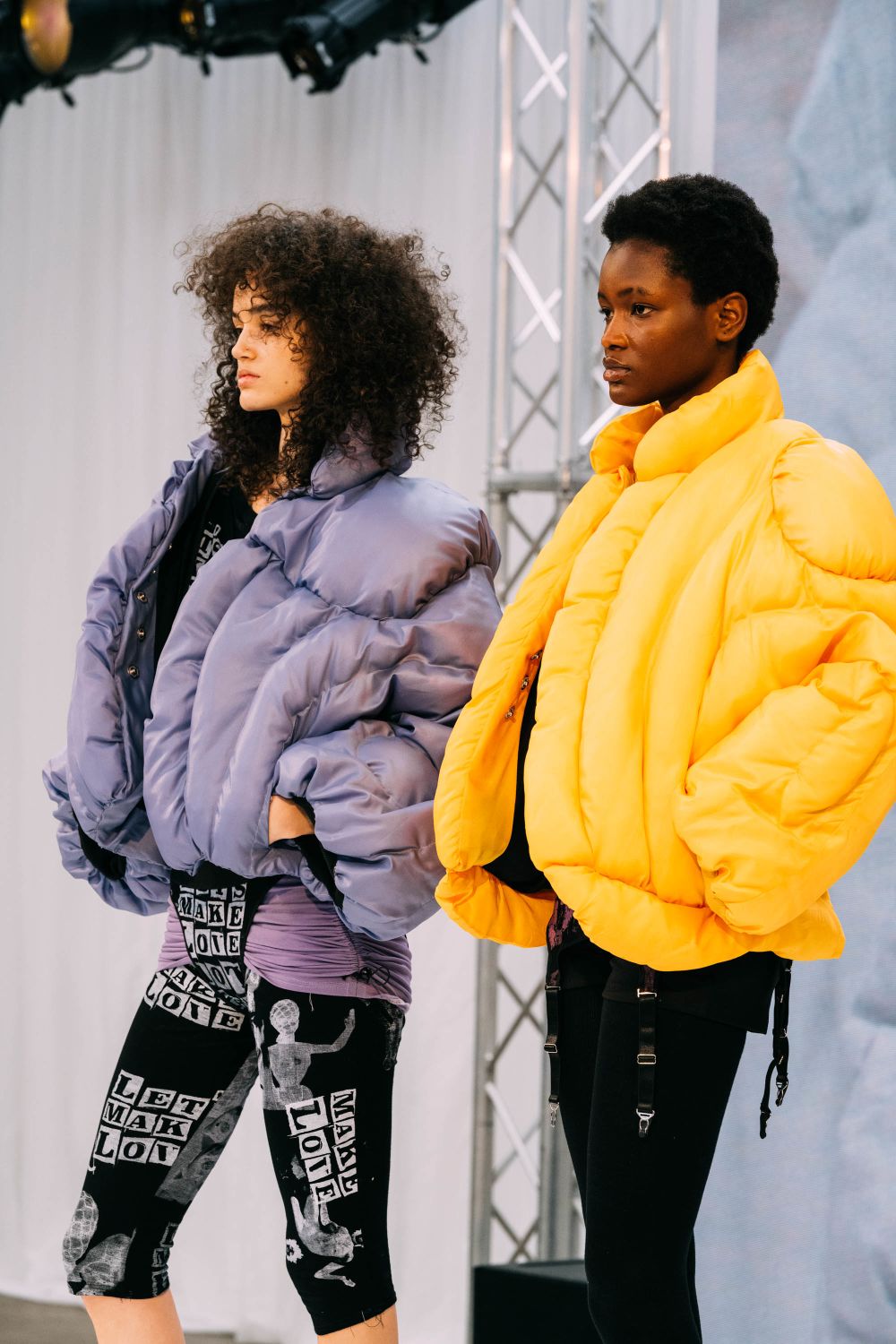 Two models on stage, wearing purple and orange puffer jackets