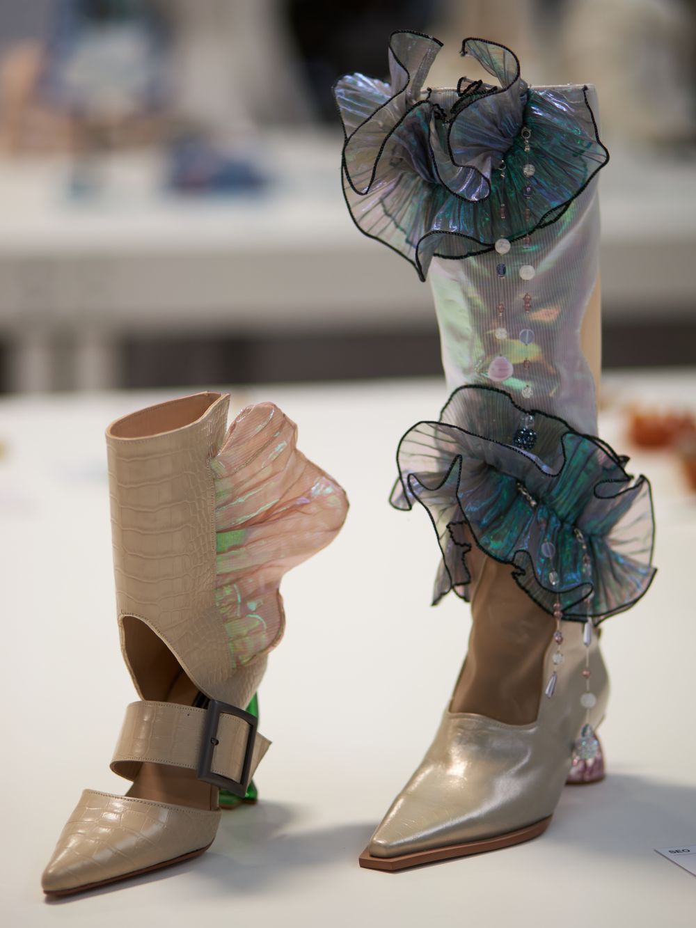 Two footwear items, left a shorter beige and pearl colour, the right a taller boot with blue frills