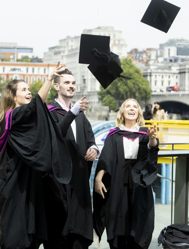 Two female and one male graduates throwing their hats in the air