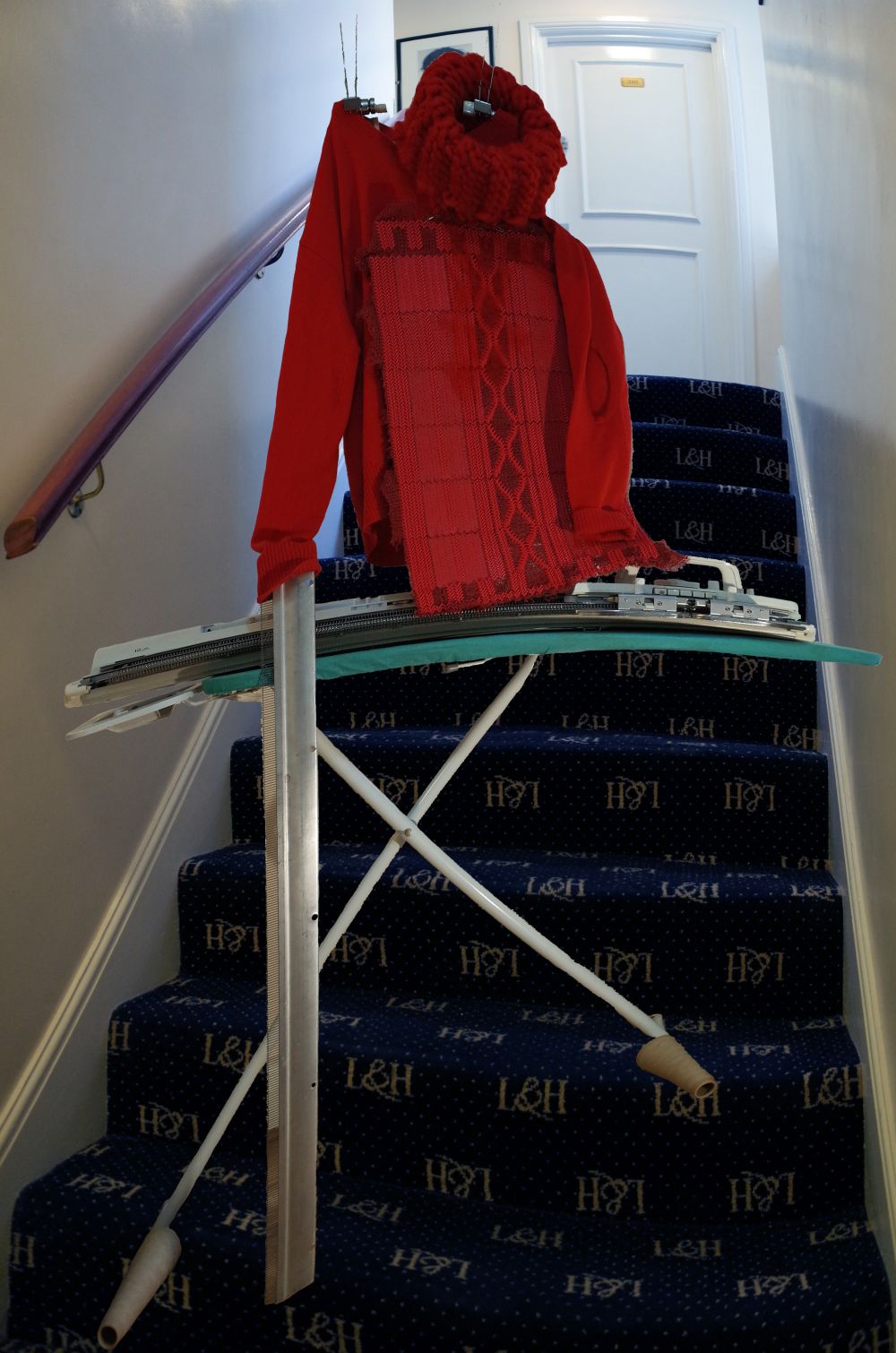 Handcrafted mannequin on staircase wearing a red knitted top.
