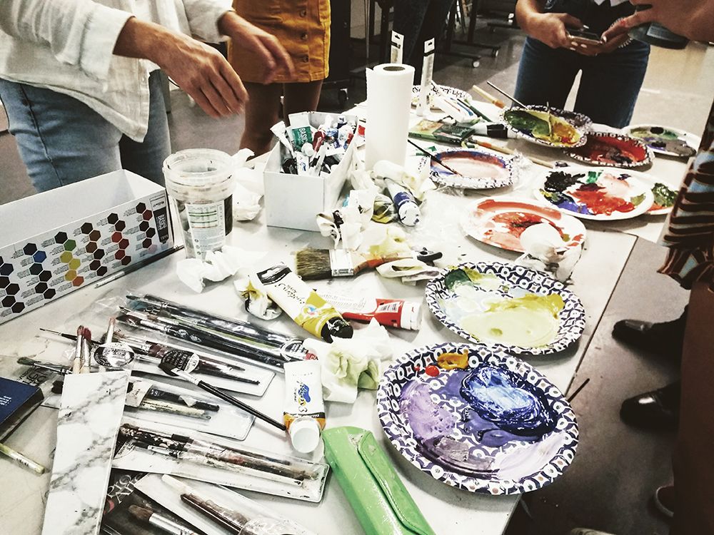 Students stood around a table filled with paint brushes and paints.