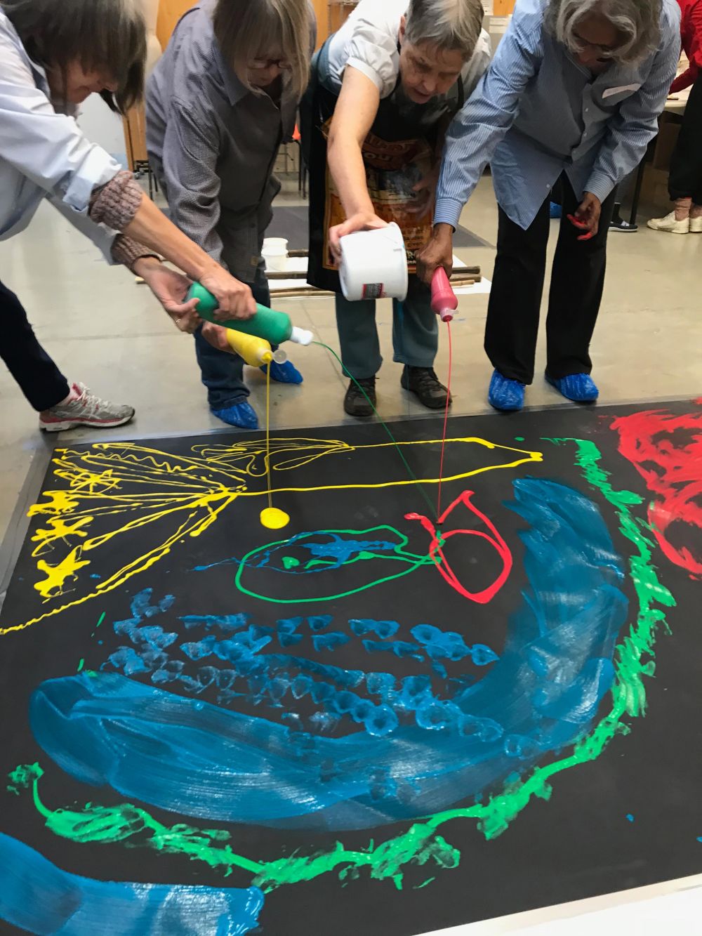 Four people pouring coloured paint onto large black canvas