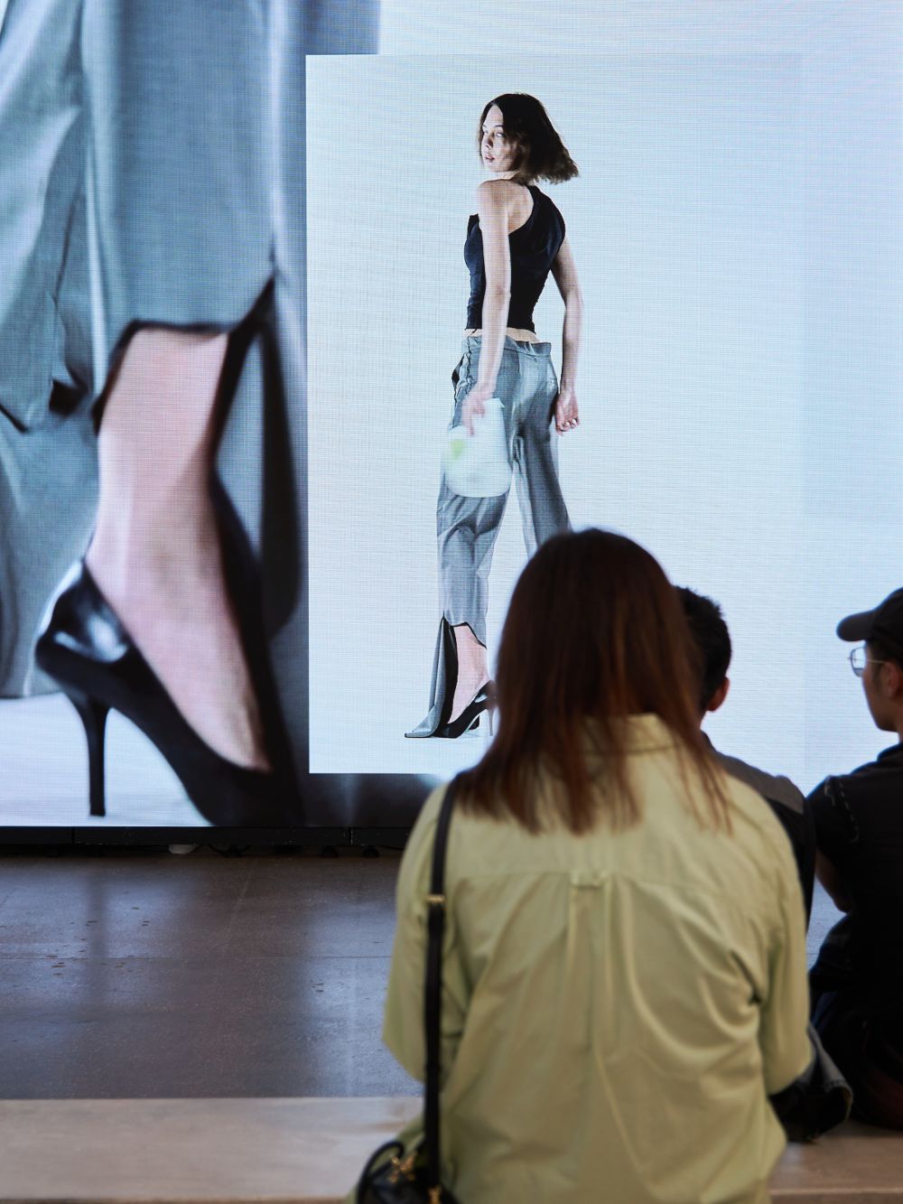 Behind the head shot of person looking at a screen where a model is wearing a look - staring into the camera