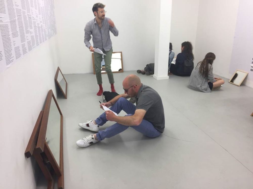 gallery installation with mirrors proped against walls and people sittin gon floor looking at themselves in the mirrors