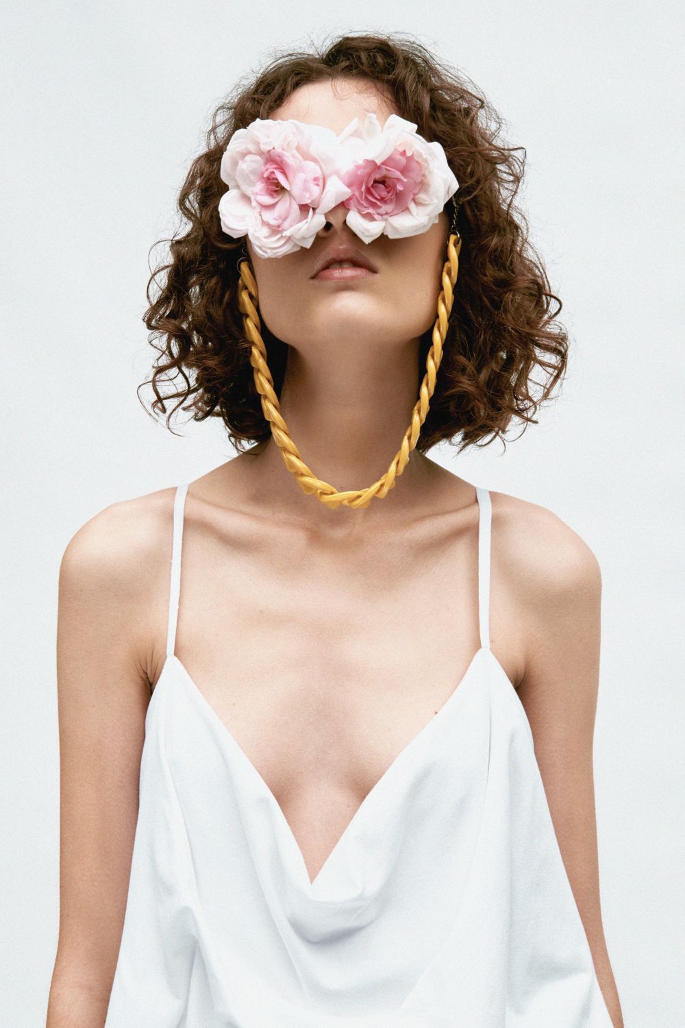 close up of model in white garment, wearing pink rose petal glasses that completely cover the eyes, with gold chain