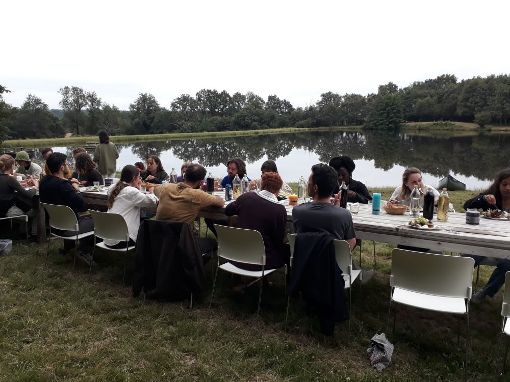 people sittoing on a very long table by a lake