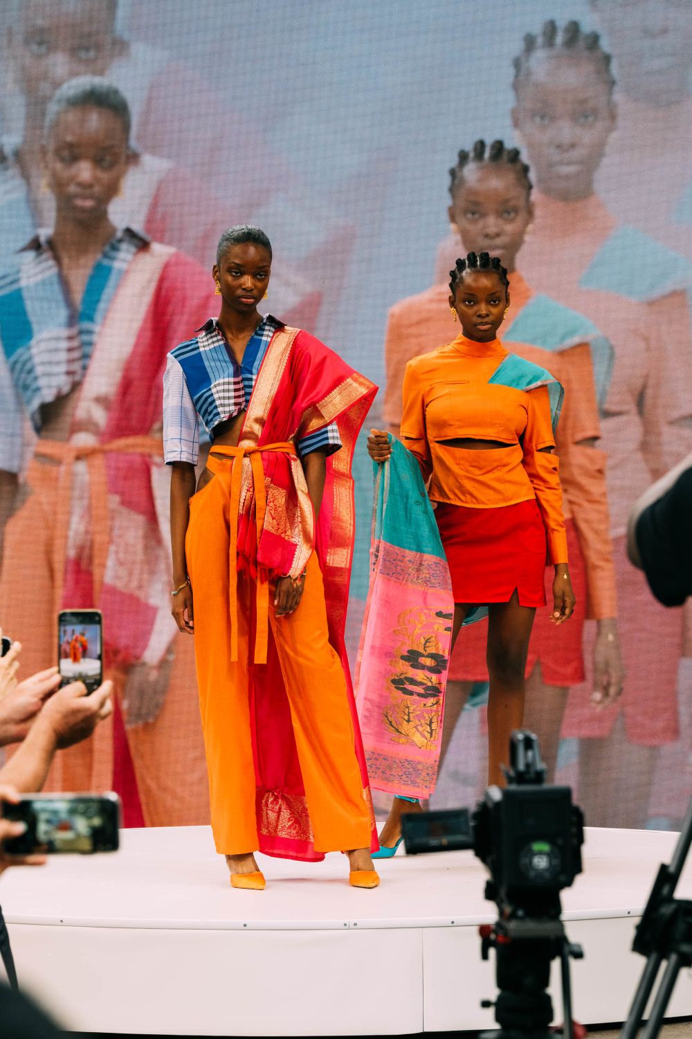 Two models on stage wearing orange, blue and teal patterns