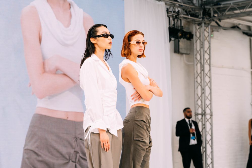 Two models on stage, wearing black backless outfits