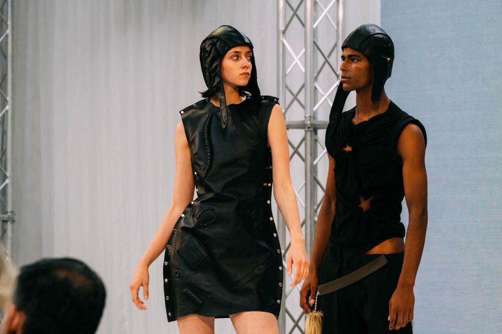 Two models on stage wearing black outfits with old flight helmets in all black