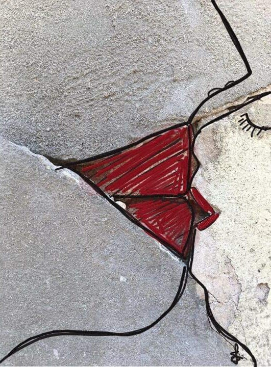 A close-up of a crack in a concrete wall which has been drawn and painted on to look like two people kissing