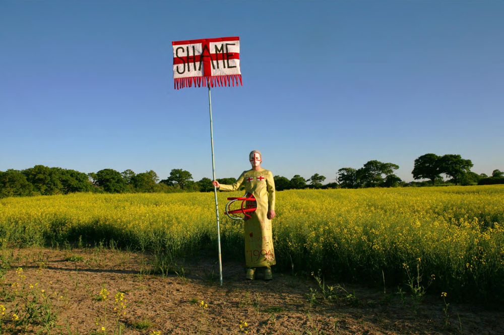 Man standing in field with St George's Cross with 'Shame' written across
