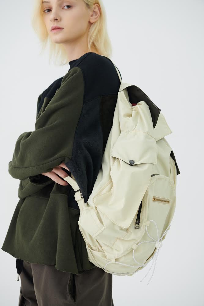 Model with blonde hair wearing a cream backpack