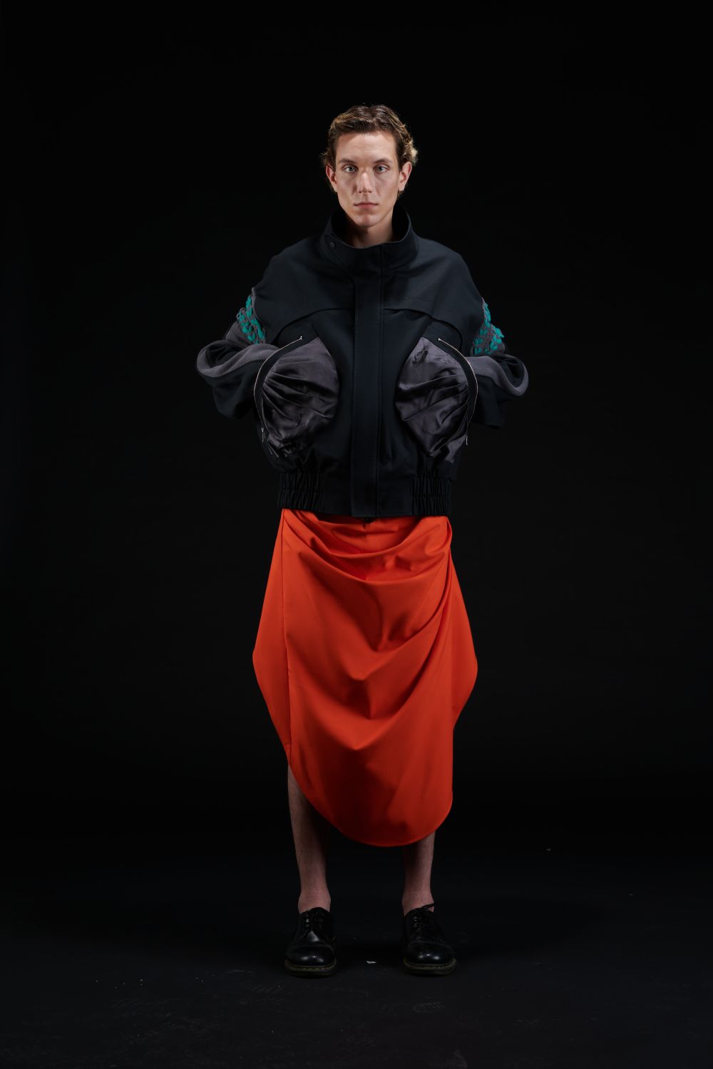 Male model in black top with covered hands and red skirt.
