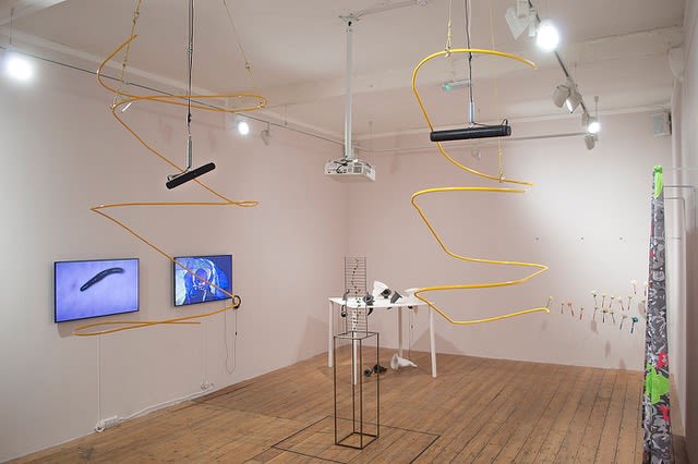 An exhibtion in a gallery with screens and yellow metal sculptures