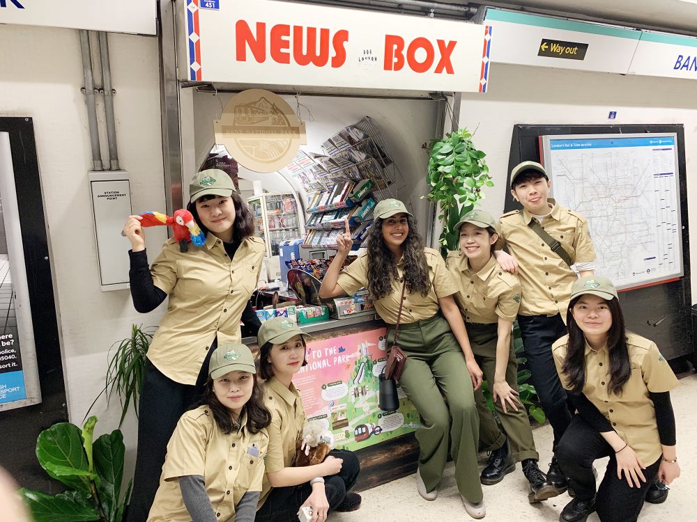 Students dressed as park rangers stand outside a news kiosk at bank station