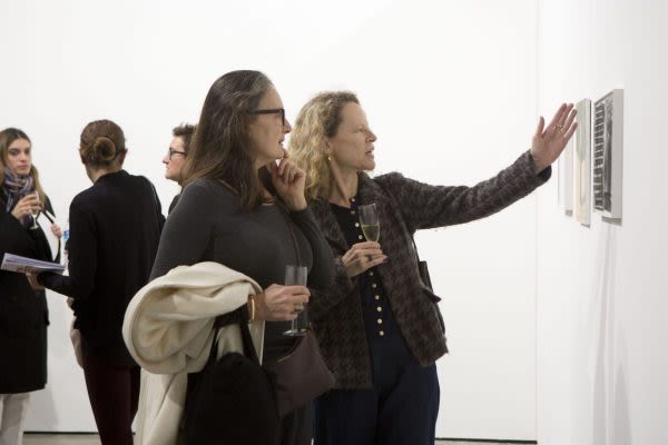 Two women looking at artwork hung on a wall, one of them gesturing towards the work in mid discussion