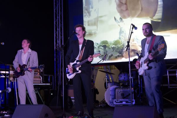 Photograph of three men on stage in suits, performing with guitars