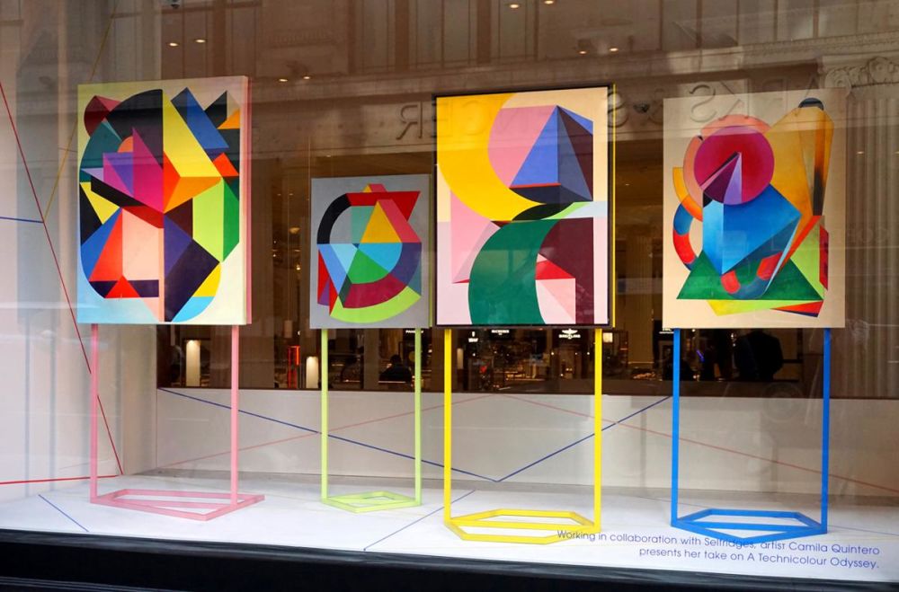 Four colourful and geometric paintings on colourful metal stands, being displayed in a shop window