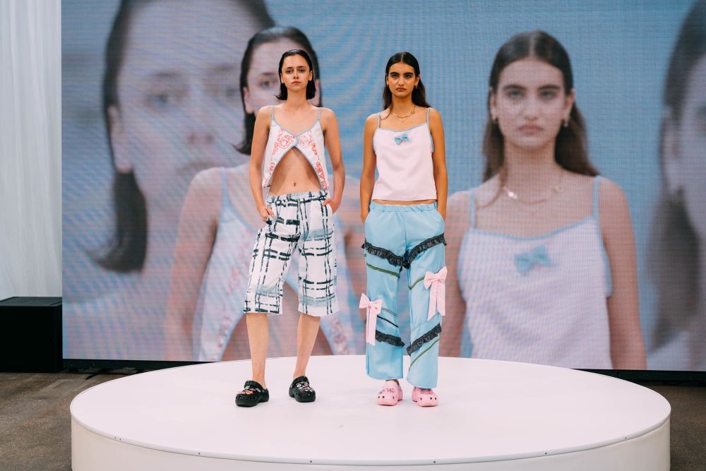 Two models on stage, left wearing white pants, the right wearing sky blue pants