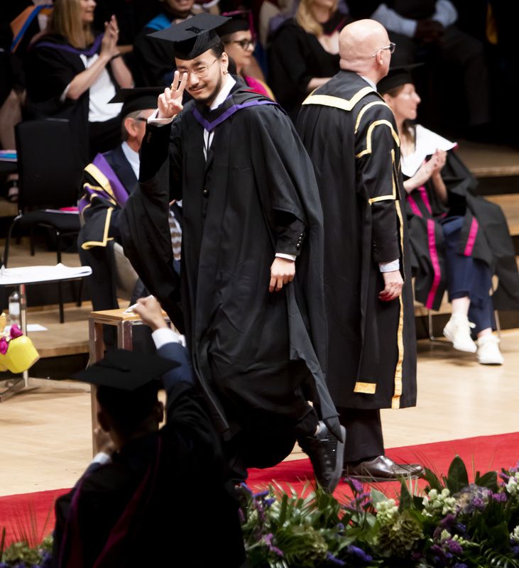 Male graduate walking across the ceremony stage and giving a 'peace' sign to the camera