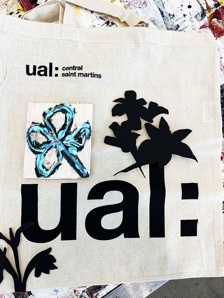 Fabric with UAL logo customized with blue flower painting and additional floral shaped material on top of logo lettering.
