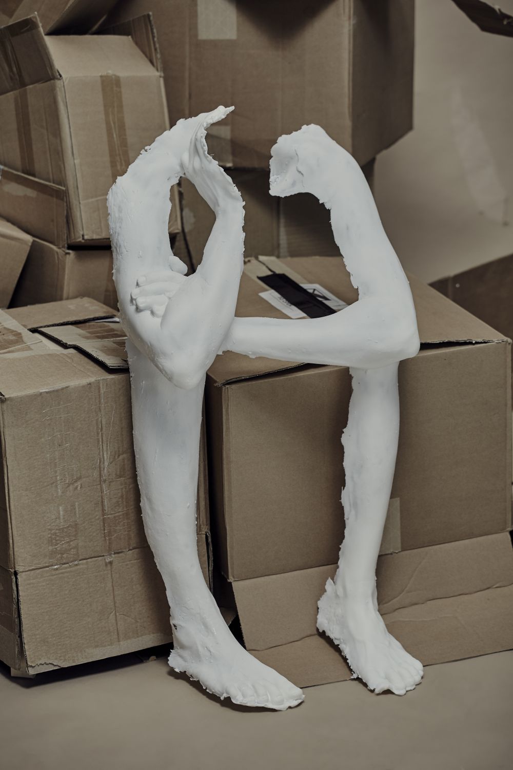 artefact limb cast, crossed arm slumped forward, 'sitting' on a pile of cardboard boxes