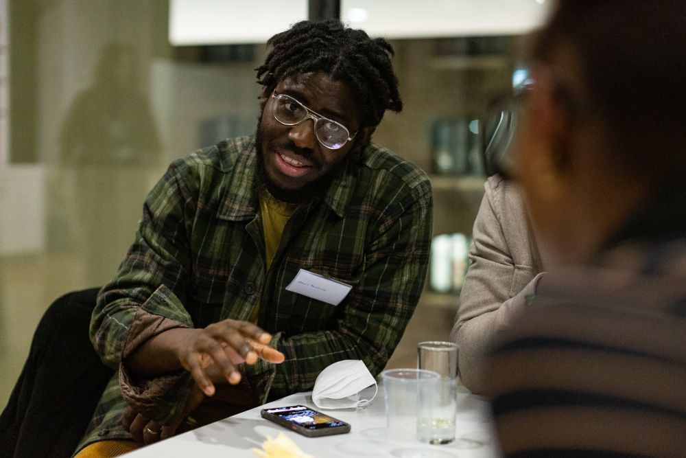 A man talking. He's wearing a checked shirt and glasses 