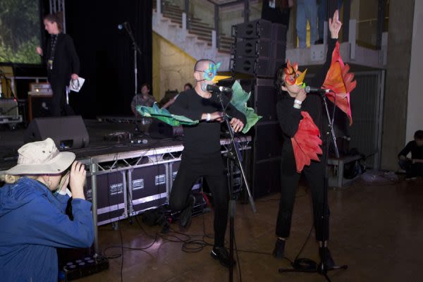 Photograph of two people dressed in bird costumes dancing and singing into microphones