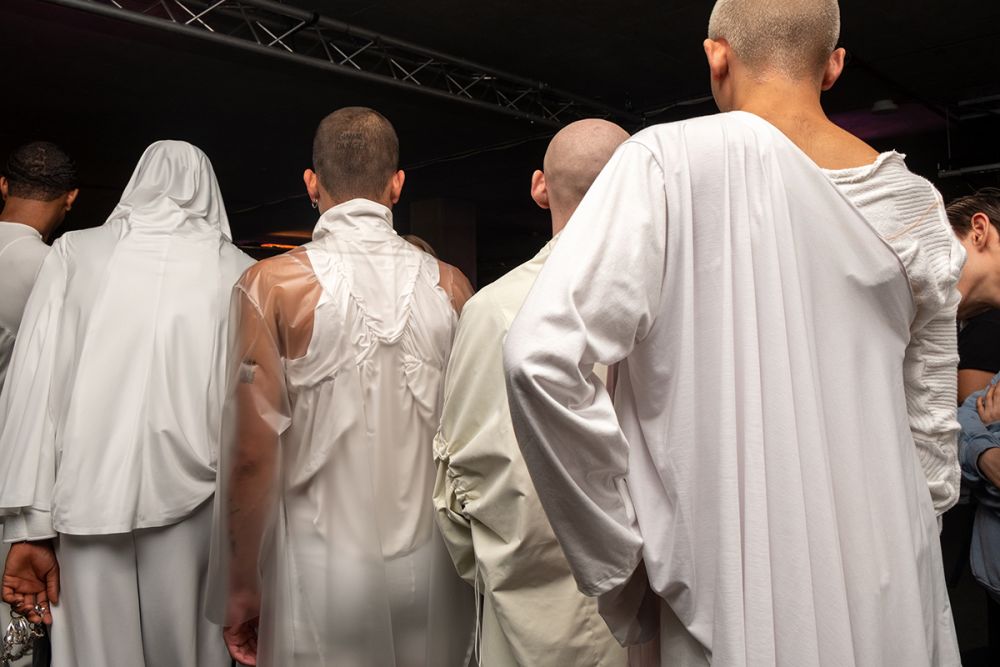 A line of male models with their backs turned all wearing white