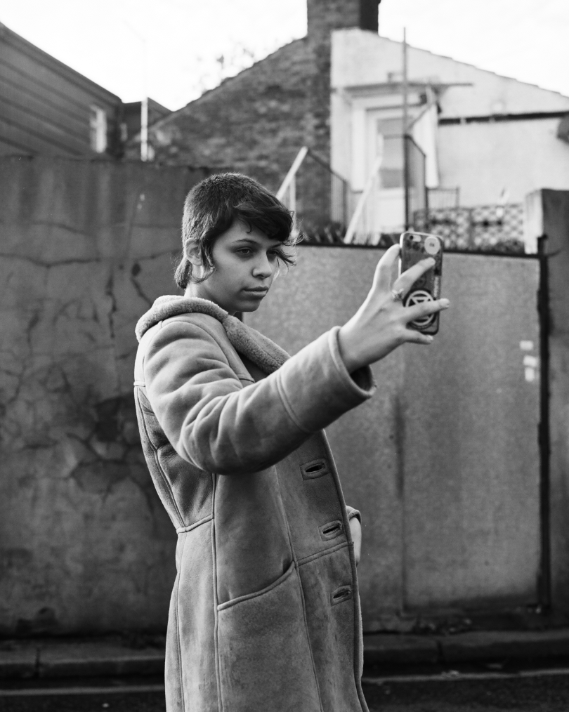 Photograph of a young woman holding up a phone to take a selfie