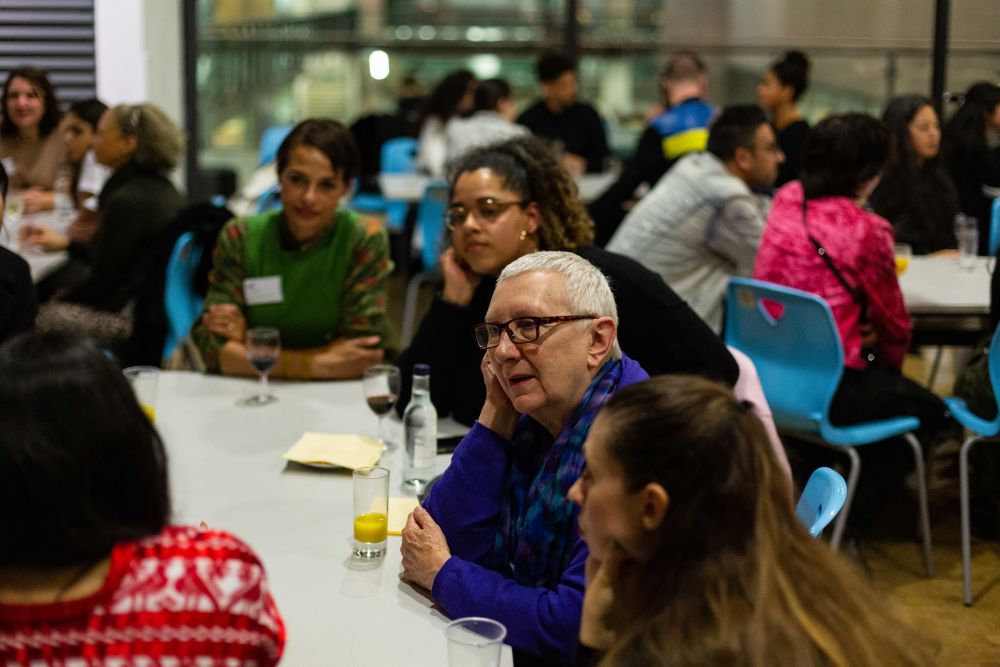 People sat around tables in large groups, chatting and listening 