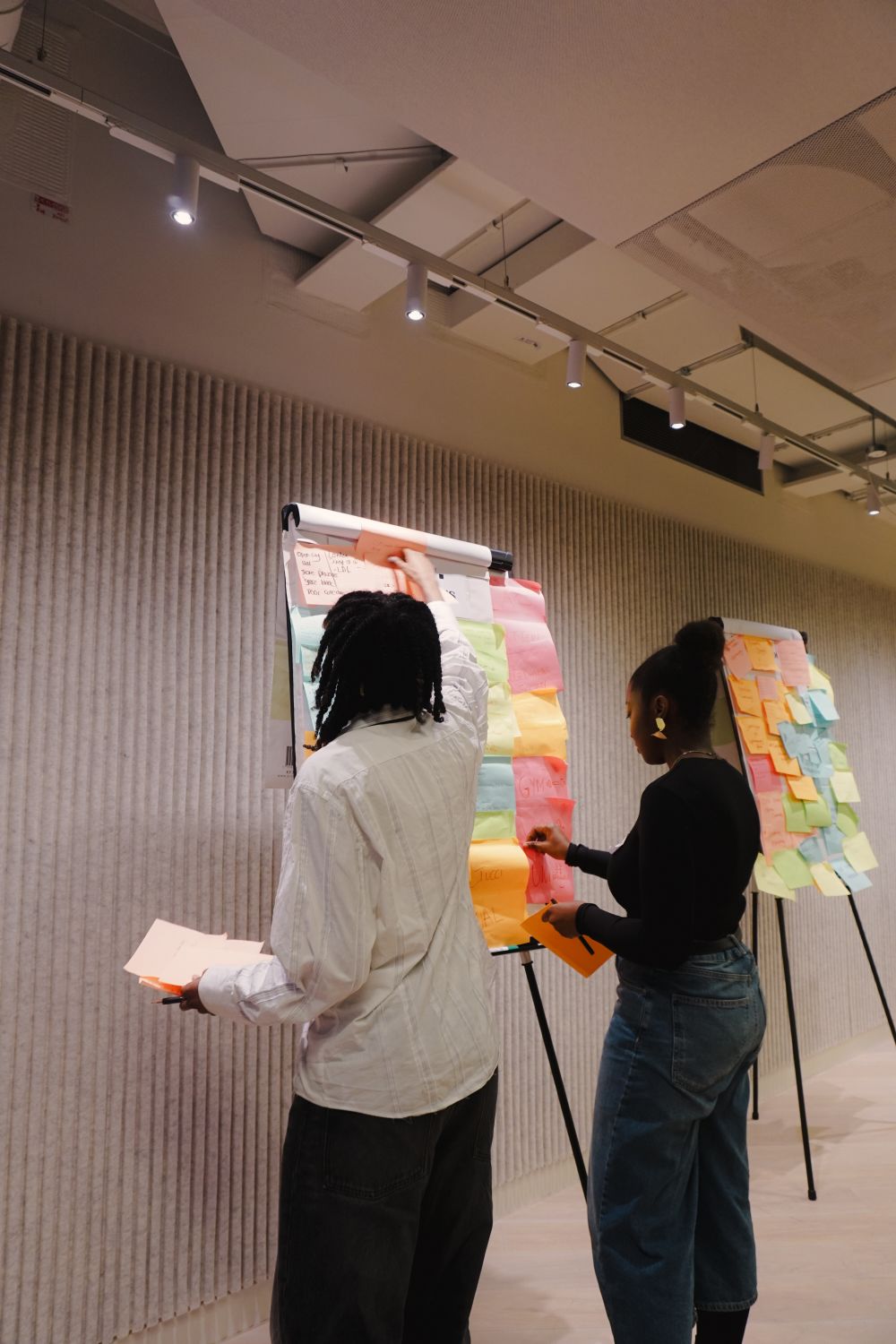 Two people writing on a white board covered in post-its