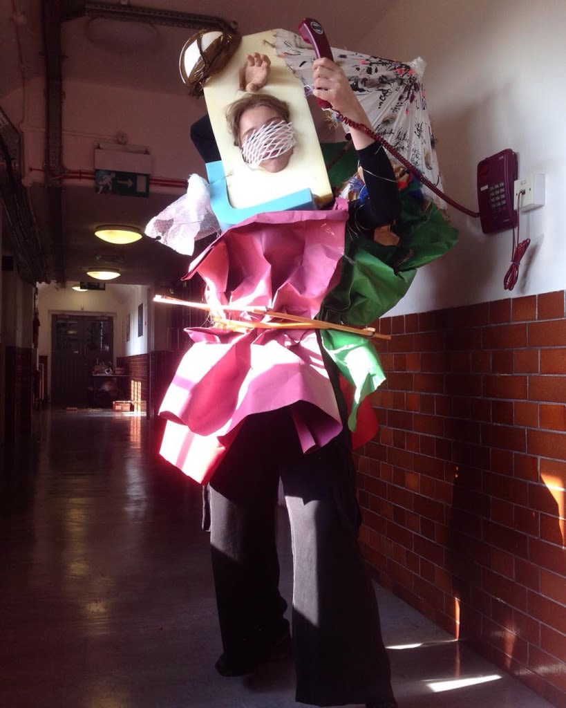 Student experimental outfit made of rubbish standing in a tiled corridor