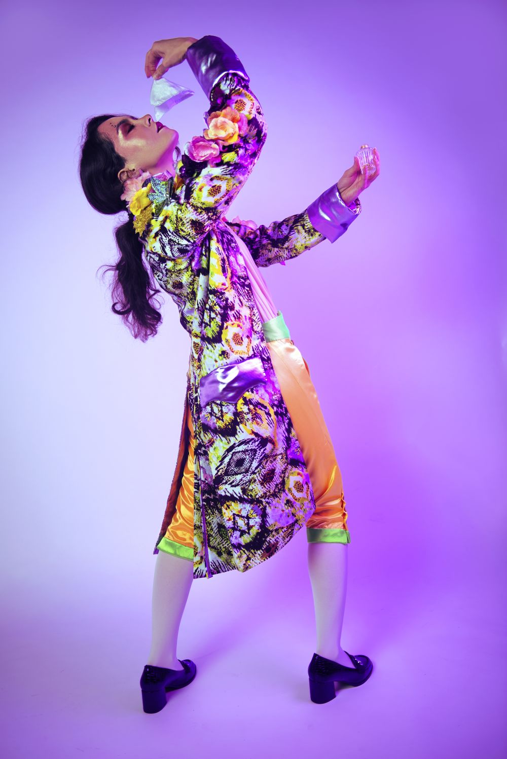 Student in colourful dress behind purple background with perfume bottle.