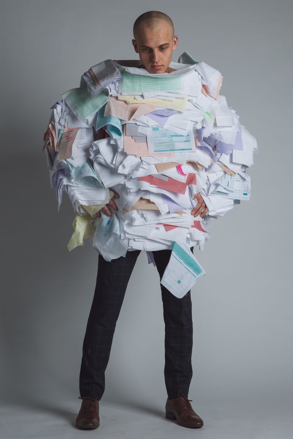 model standing in oversized garment with layered rough fabric that looks like piles of papers, application forms and bills.