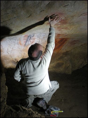 Professor Paul Pettitt reaches towards a hand stencil on a cave wall
