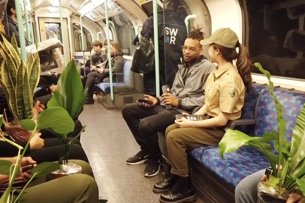 A student dressed as a park ranger speaks to a man on a tube train