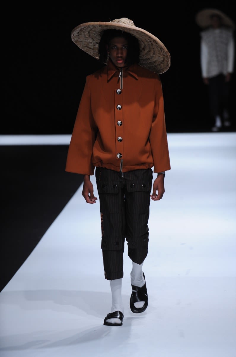 Male model wearing orange blouse black trousers and hat designed by Christele Mbosso 