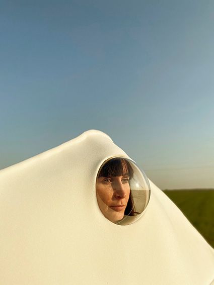 Close up portrait of woman wearing voluminous white covering with face looking out of circular window-like feature
