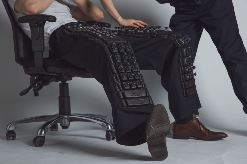 close up of model sitting in a chair, wearing trousers embellished with black embossed keyboard cut out letters and console knobs.