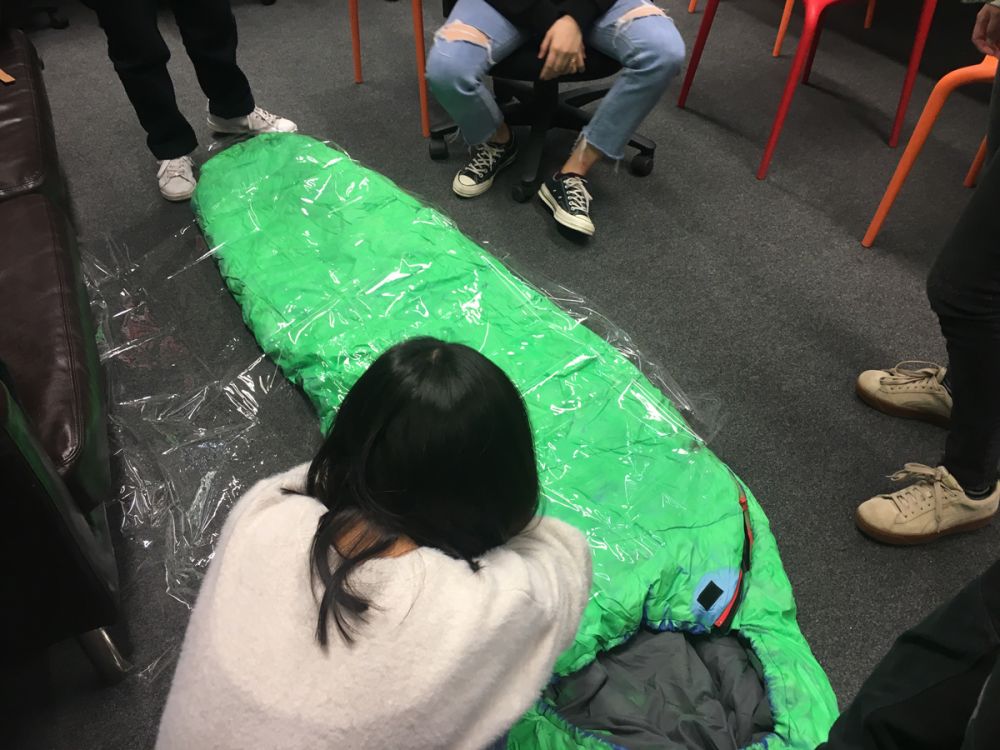 Students work in progress, wrapping a green sleeping bag in clear plastic