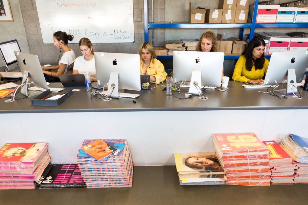 Students working at computers with piles of publications in the foreground