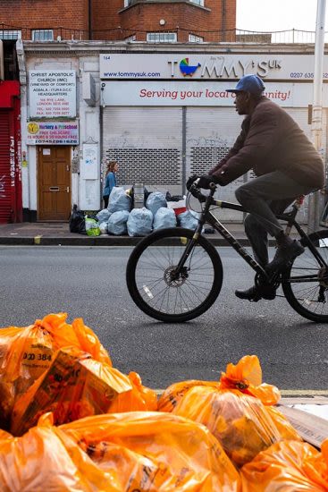 a man cycling past a pile of orange bin bags in the street